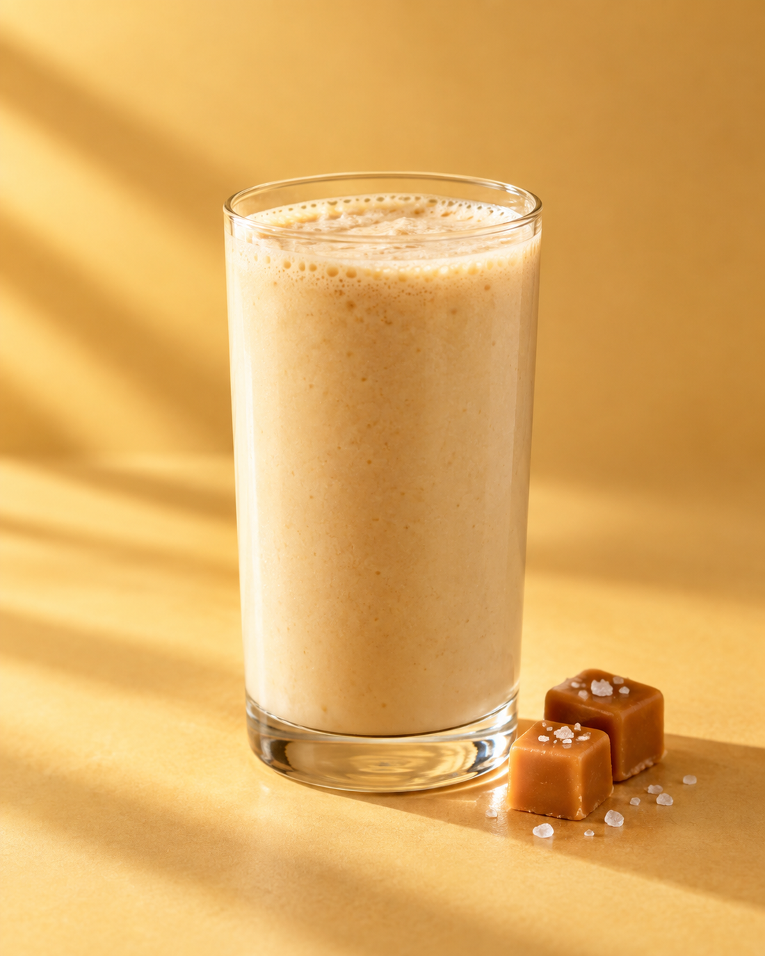 Salted caramel serving inspiration: a creamy shake in a clear glass with caramel cubes and salt crystals.